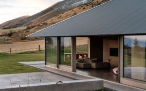Exterior view of a modern home with polished concrete patio and large sliding glass doors surrounded by rural landscape.